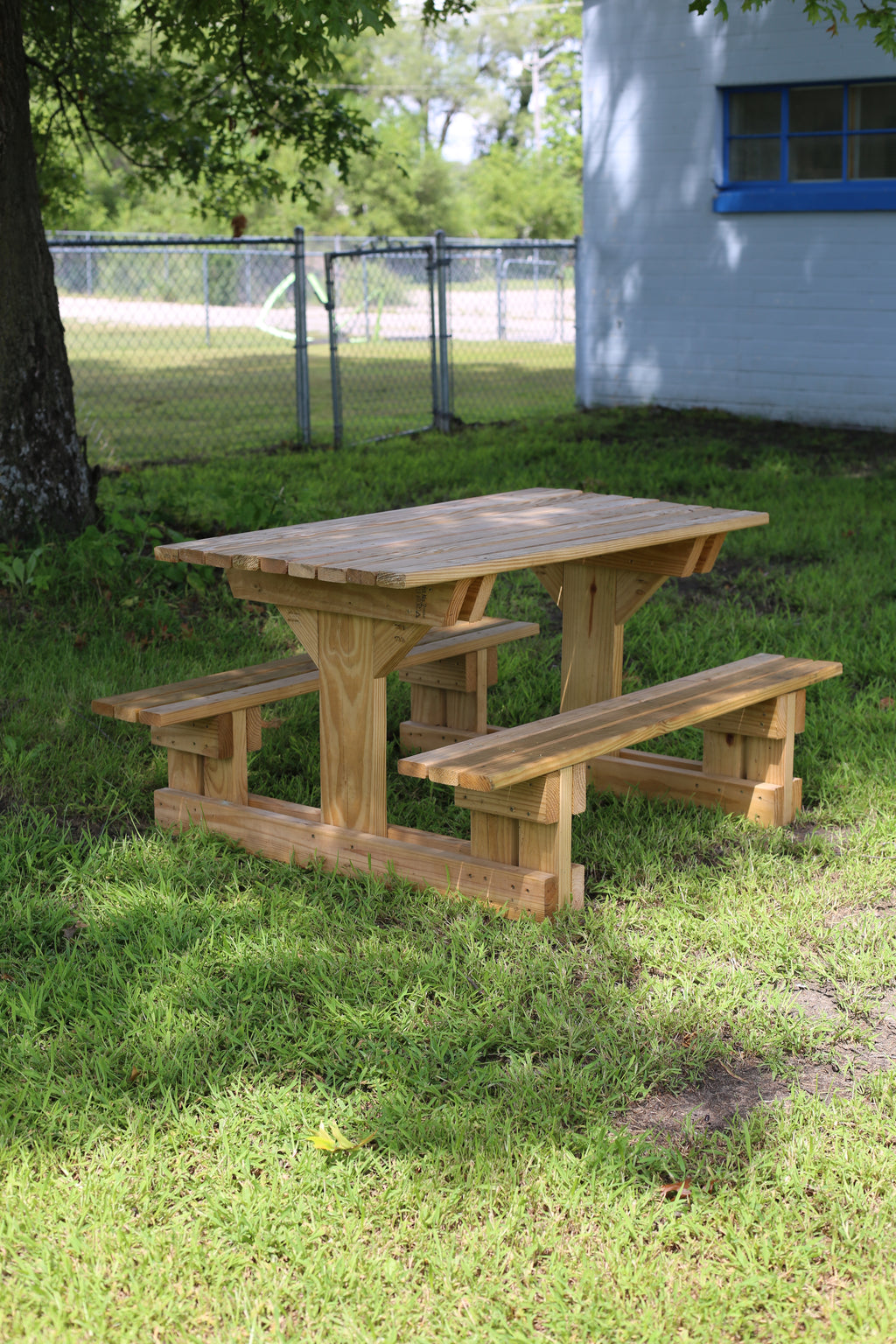 Wooden picnic table on grass with a building and fence in the background