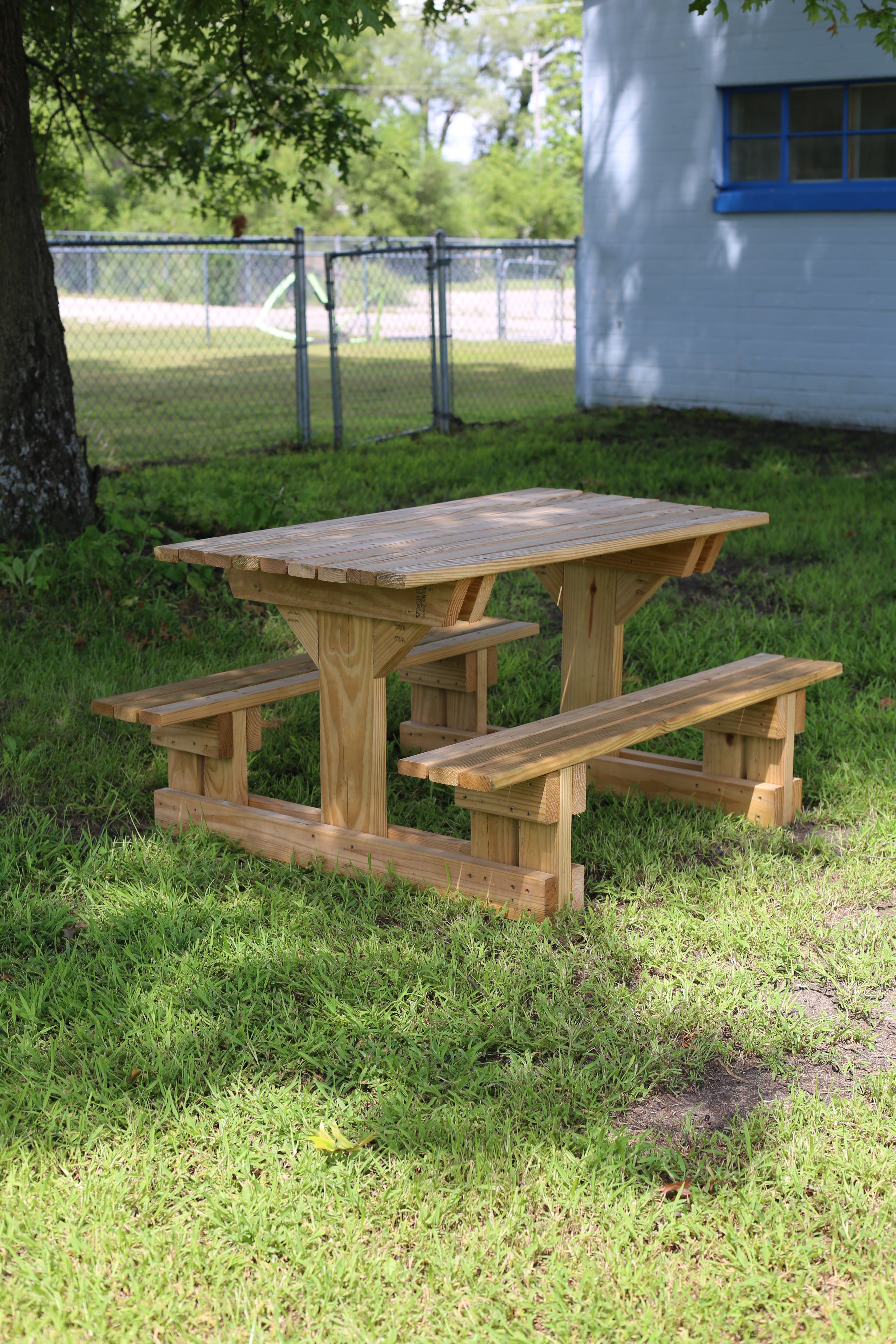Wooden picnic table on grass with a building and fence in the background
