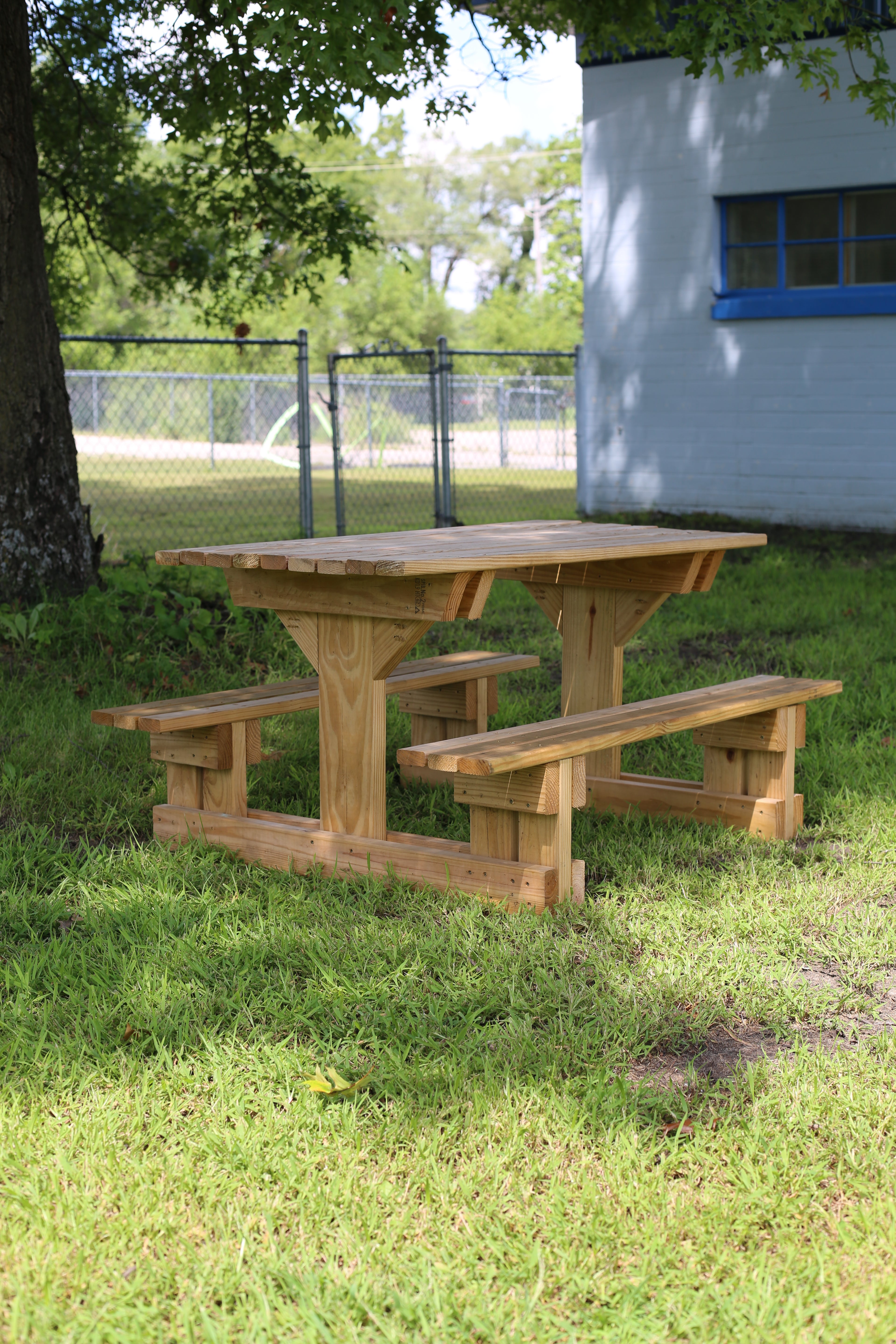 Wooden picnic table on grass with a house and trees in the background