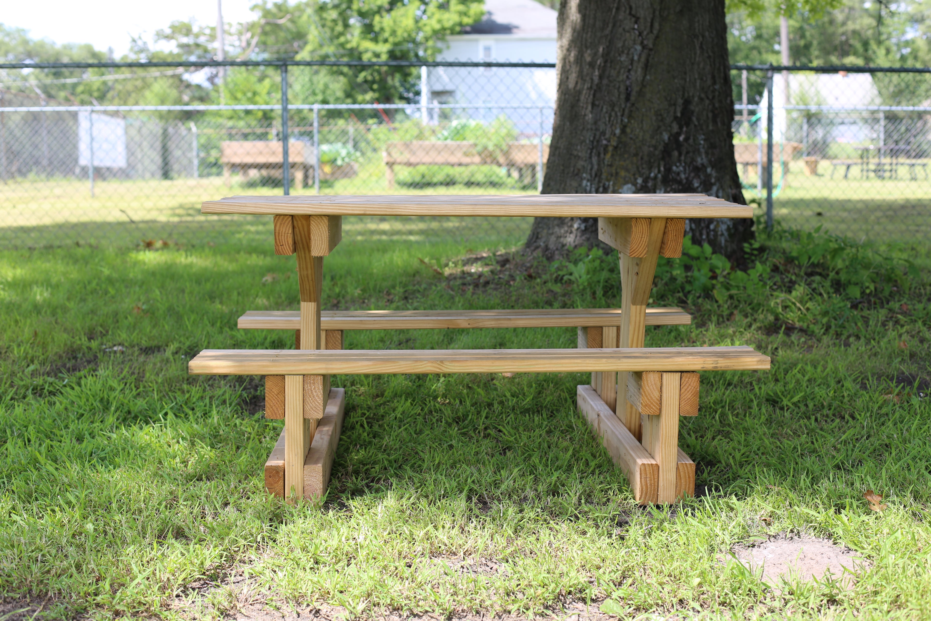 Wooden picnic table in a park setting with grass and trees.